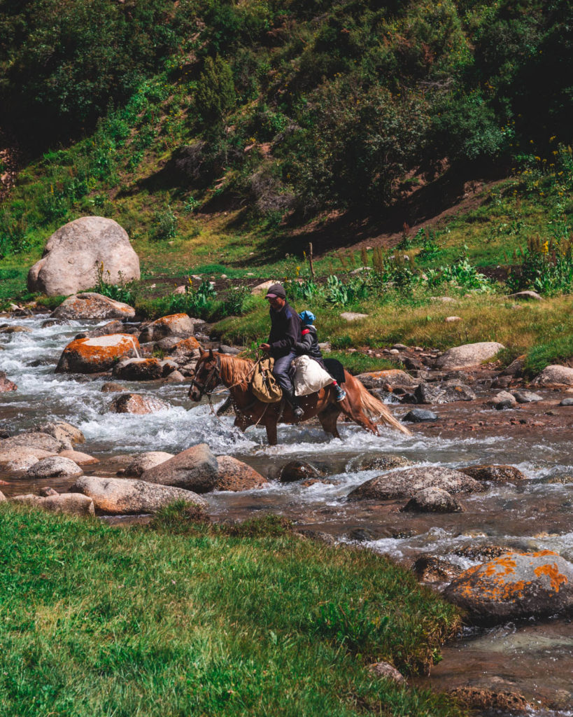 Local Kyrgyz nomad crossing the river with on a horse